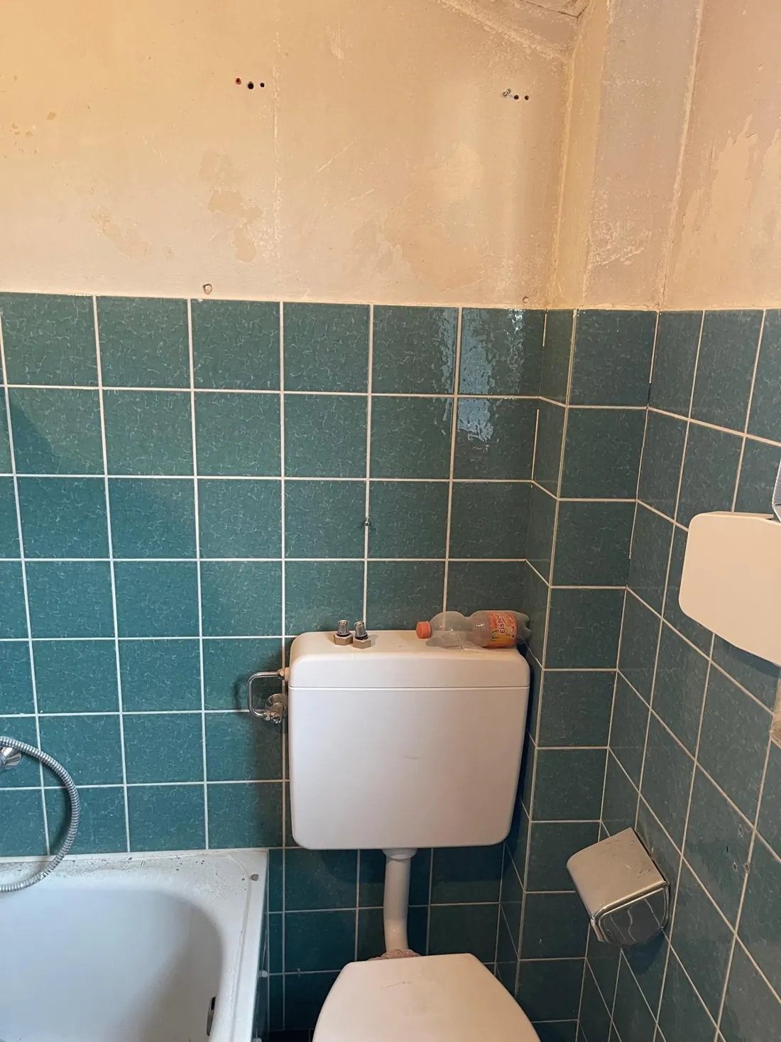 Altes Bad im Dachgeschoss mit grünen Fliesen, Badewanne und Spülkasten auf der Wand