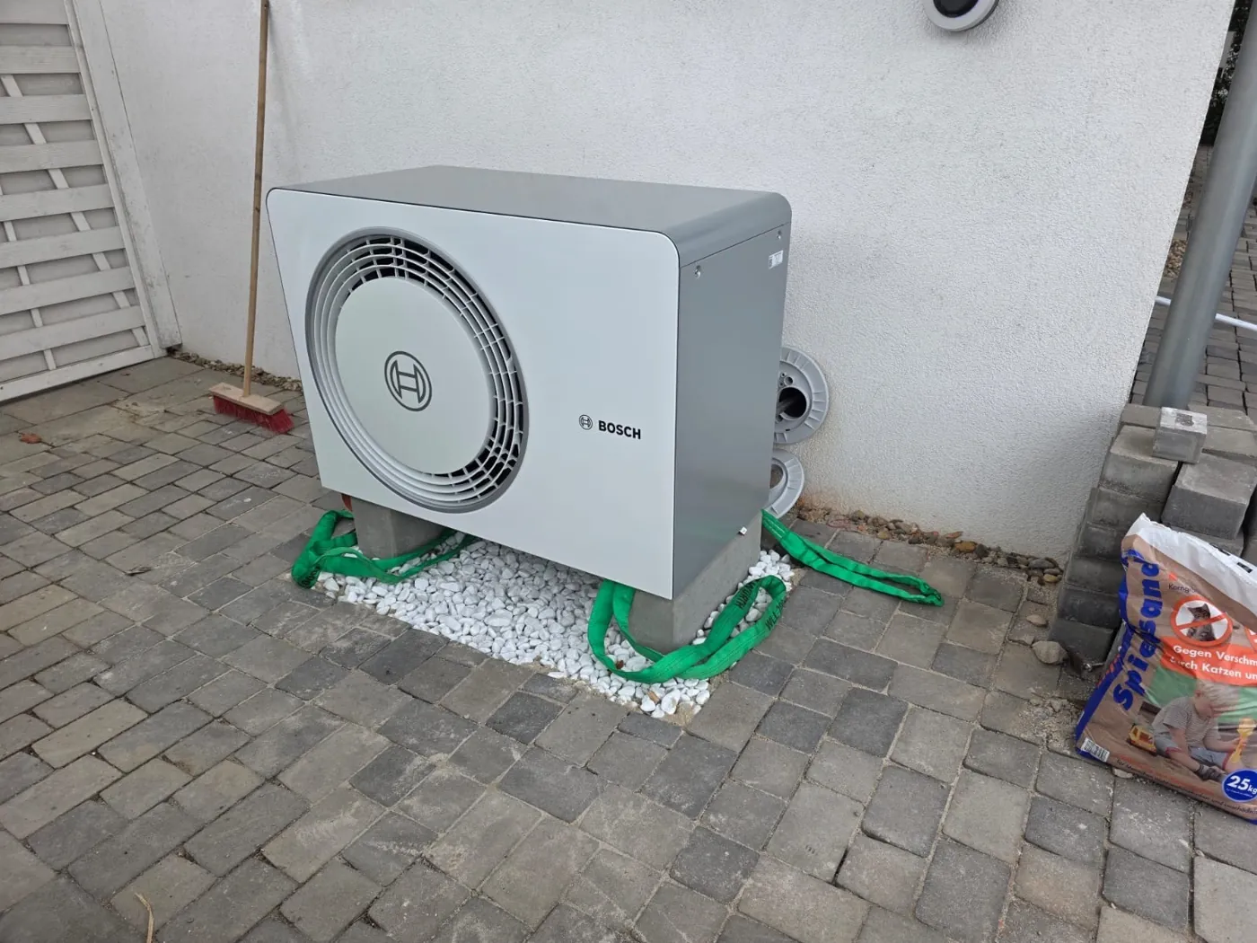 Bosch-Außengerät nach dem Absetzen auf zwei Betonsockeln mit Hebegurten und hellem Kies