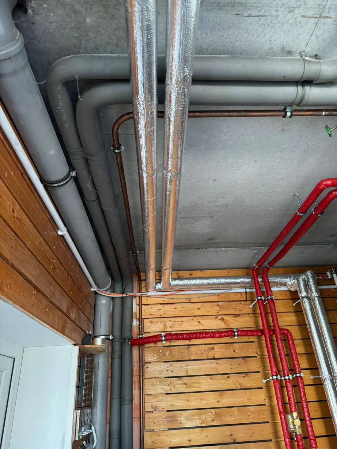 Silbern und rot gedämmte Leitungen unter der Betondecke