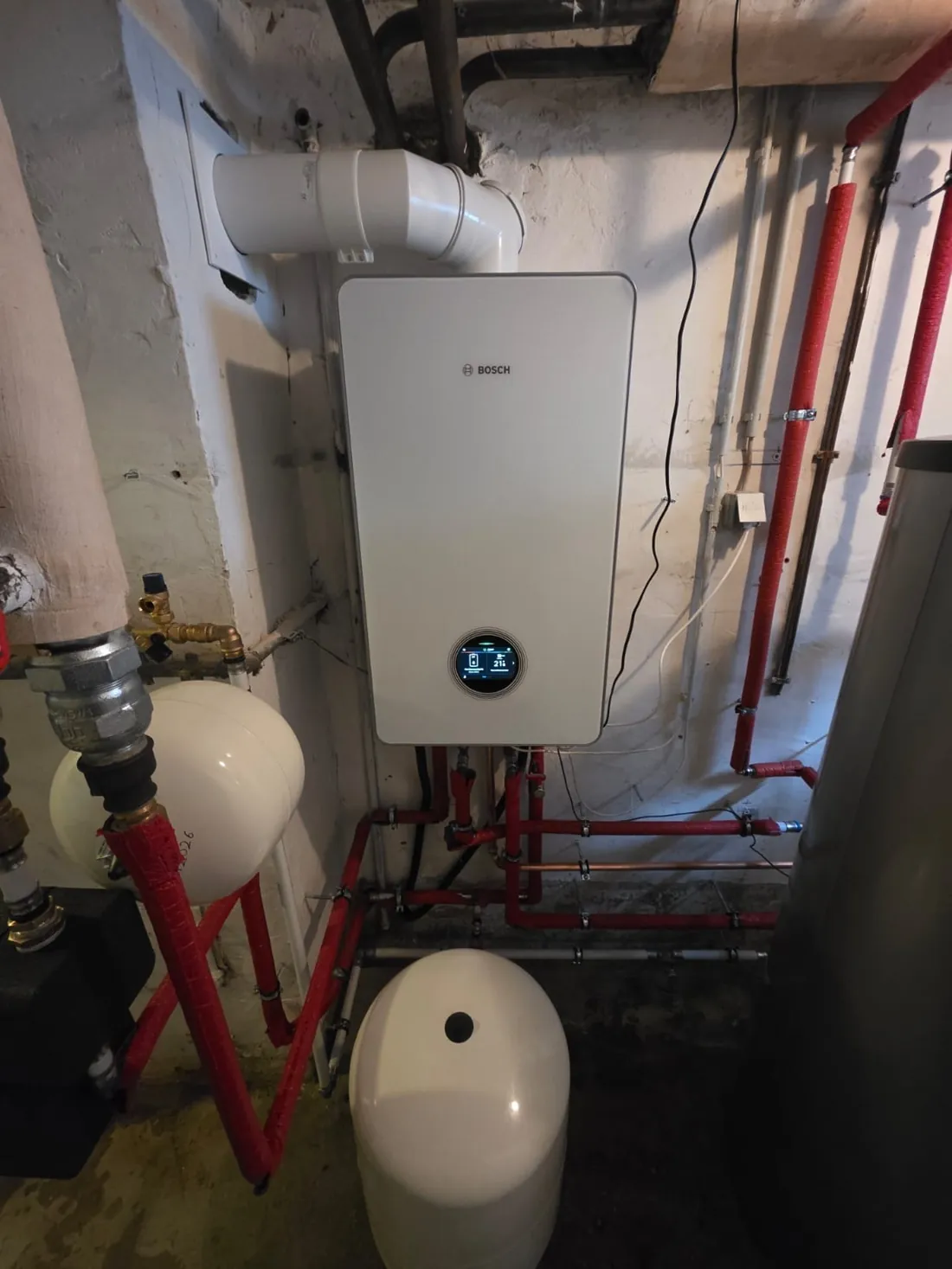 Bosch Gas-Brennwertgerät mit rundem Display und rot gedämmten Leitungen in einem Altbaukeller in Lindenberg